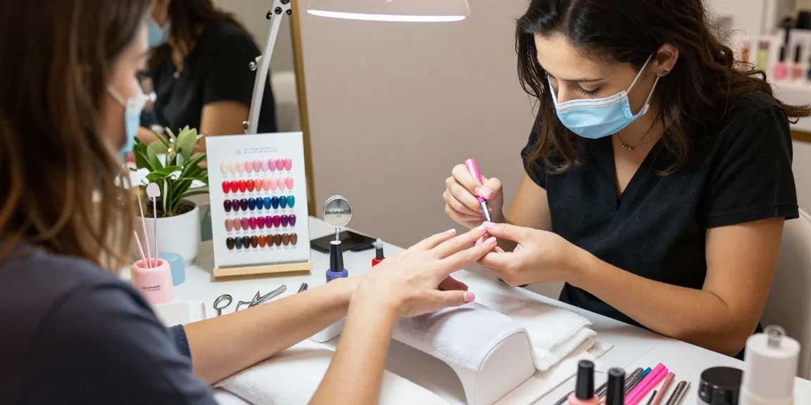 Aplicarea ojei semipermanente într-un salon de înfrumusețare profesional, cu culori vibrante de lac de unghii.